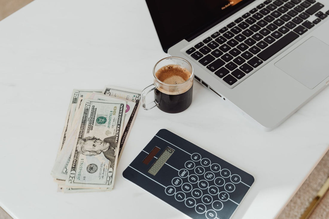 Laptop, calculator, cash and coffee on a desk, working out a monthly Google Ads budget