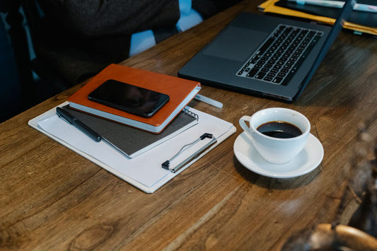 Open laptop and a cup of coffee on a wooden table next to notebooks