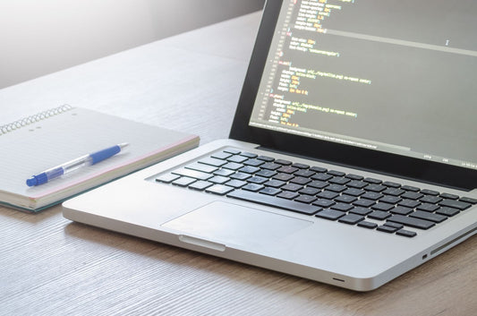 Laptop displaying website code beside a notebook, representing the work behind building a website