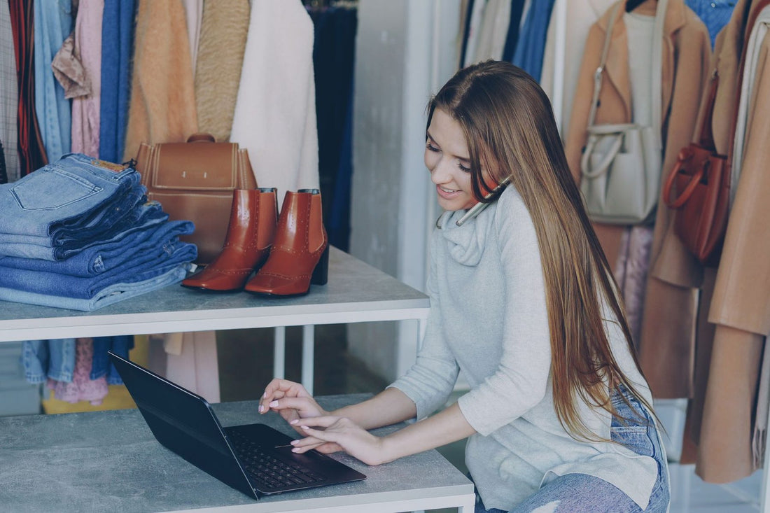 Boutique owner working on a laptop between clothing racks, running her own marketing on a small budget